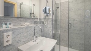 A modern bathroom with a white sink, a mirror, a glass shower enclosure, and marble walls. - Comfort Double Room - Logierhaus Oystercatcher (Norderney)