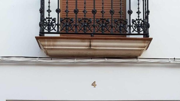 A double wooden door with a glass window, a balcony with wrought iron railings, and a small stone ledge in front. - Tourist apartments (Mota del Cuervo)
