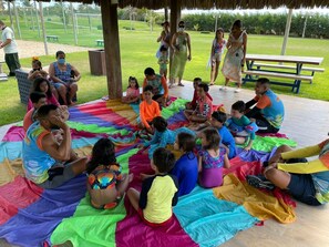 A group of children and adults sitting on colorful mats in a circular arrangement outdoors. - BEACH LIVING APARTMENTS (Porto das Dunas)