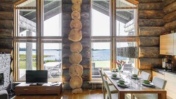 L’intérieur d’une cabane en rondins comprend un coin repas, une cuisine et une grande fenêtre donnant sur un plan d’eau.