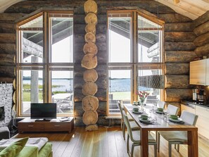 A log cabin interior with a dining area, kitchen, and a large window overlooking a body of water. - Villa pärla by Interhome (Olhava)