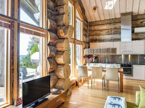 A log cabin interior with a dining area, kitchen, and a large TV. - Villa pärla by Interhome (Olhava)