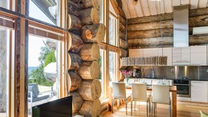 A cozy log cabin interior with a dining area, kitchen, and a large window overlooking a scenic view. - Villa pärla by Interhome (Olhava)