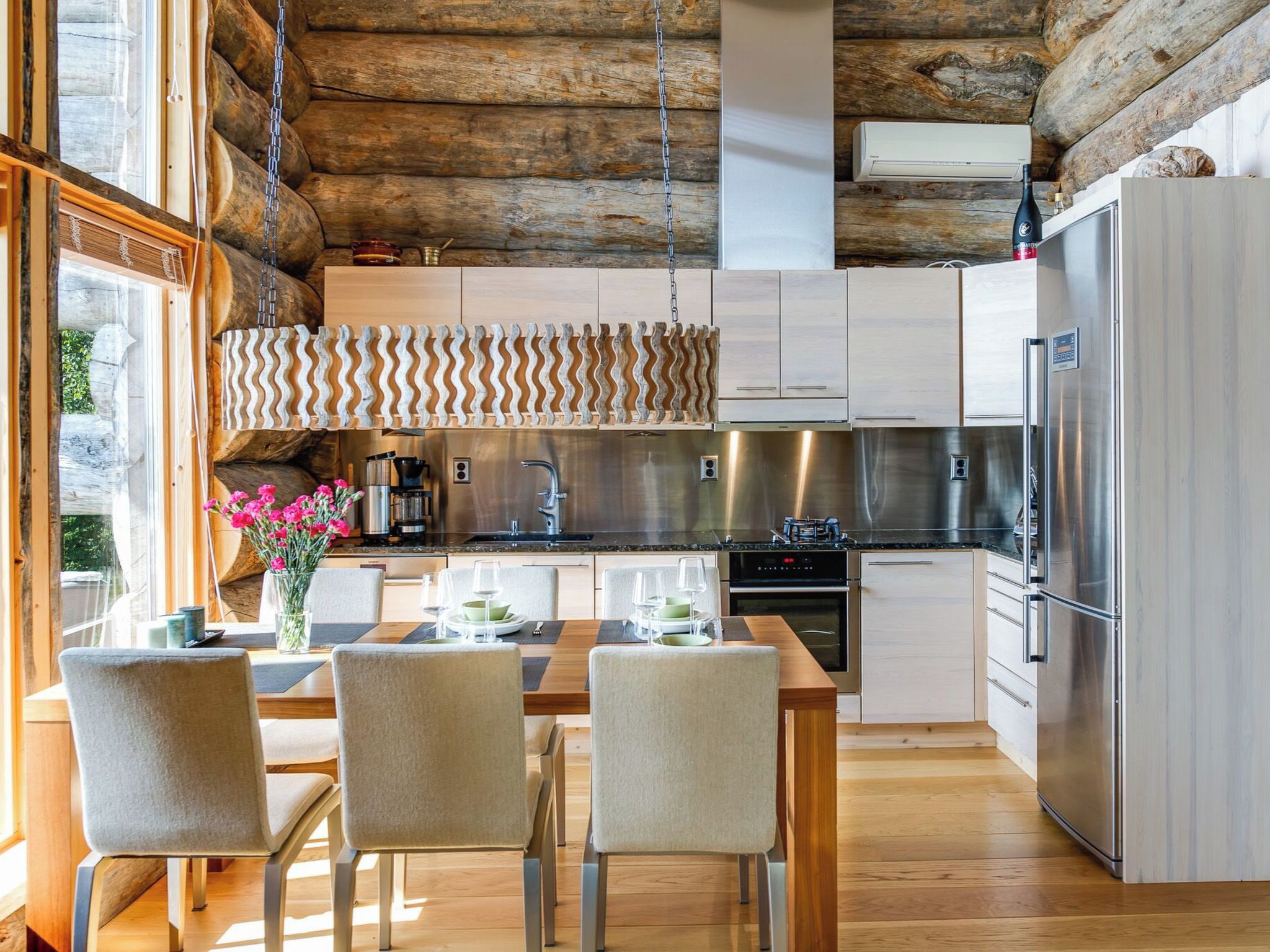 Une cuisine moderne avec un plafond en bois, des appareils électroménagers en acier inoxydable et un coin repas comprenant une table et des chaises.