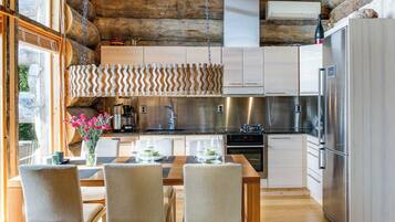 Une cuisine moderne avec un plafond en bois, des appareils électroménagers en acier inoxydable et un coin repas comprenant une table et des chaises.