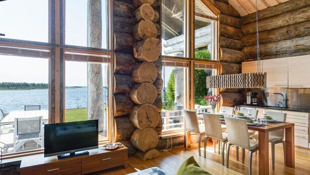A log cabin with a large window overlooking a lake, a dining area with chairs and a table, and a kitchen with modern appliances. - Villa pärla by Interhome (Olhava)