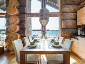 A wooden dining table set for six with a view of a lake through large windows. - Villa pärla by Interhome (Olhava)