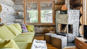 A cozy log cabin interior with a green sofa, a fireplace with a stone surround, and a window with wooden shutters. - Villa pärla by Interhome (Olhava)