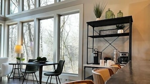 A modern dining area with a long wooden table, black chairs, and a black metal shelf with kitchen items.