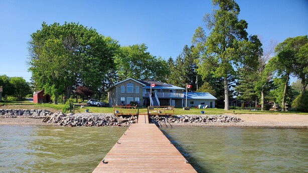 A wooden dock leading to a house with a Canadian flag, surrounded by trees and a calm body of water. - Home of 1000island#3-Directly on STL river private beach FREE boat docking (Gananoque)