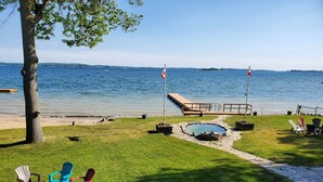 A lakeside patio with Adirondack chairs, a fire pit, and a small pool. - Home of 1000island#3-Directly on STL river private beach FREE boat docking (Gananoque)