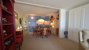A room with a dining table, chairs, a red bookshelf, a white wardrobe, and a kitchen area with cabinets and a hanging light fixture. - Edgewater House - Ocean Front Units With Spectacular Views! (Rehoboth Beach)