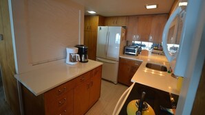 Cocina compacta con armarios de madera, un refrigerador, una cafetera y un microondas.