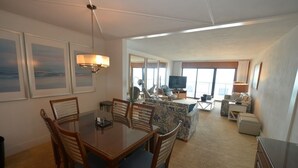 Habitación de hotel con zona de comedor, sofá, televisor y un amplio ventanal.