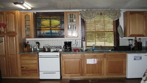 Cozinha com armários de madeira, fogão, cafeteira e janela com persianas.