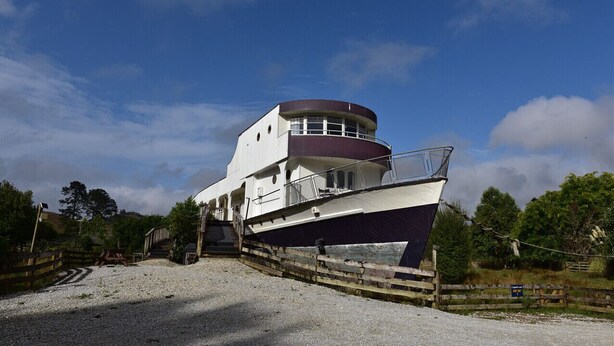 A large, multi-level boat docked at a marina with a gravel path leading to it.