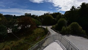 A concrete bridge with metal railings, surrounded by dense trees and a clear sky.