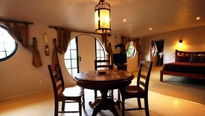 Un coin repas comprenant une table ronde en bois et quatre chaises, un lustre et un téléviseur posé sur un meuble.