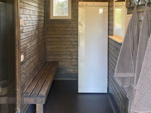 A narrow, wooden-walled bathroom with a bench, a white toilet, and a towel rack.