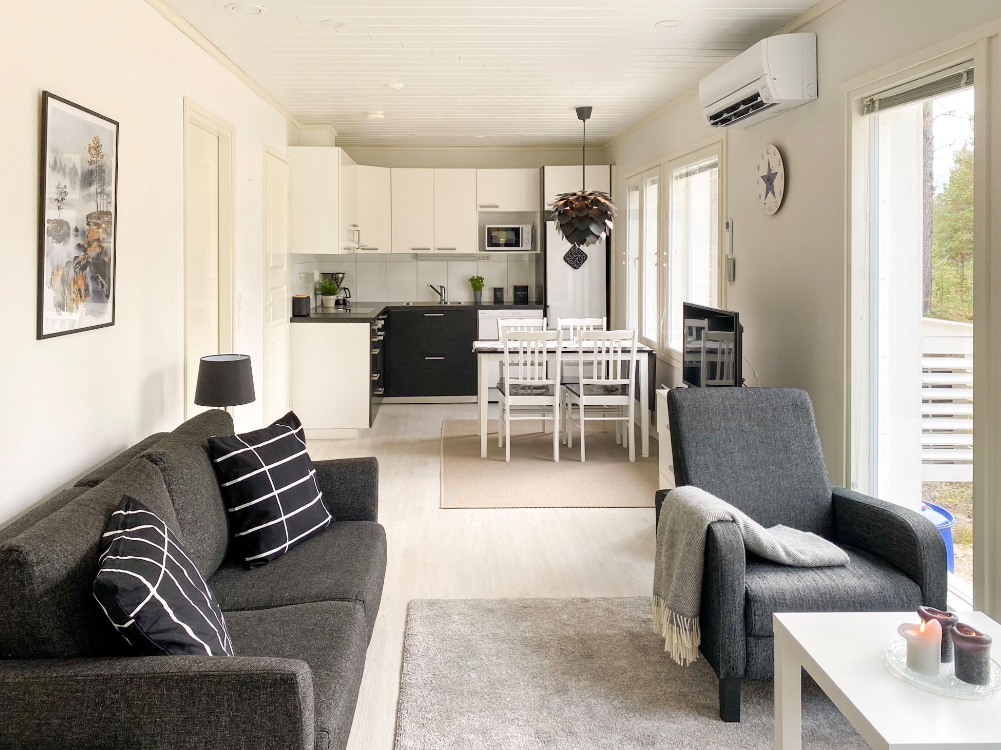 Una sala moderna con un sofá gris, una mesa de comedor con sillas y una cocina al fondo.
