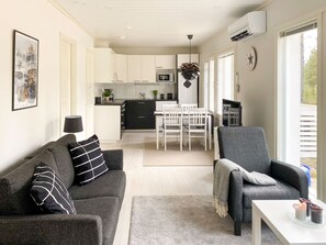 Una sala moderna con un sofá gris, una mesa de comedor con sillas y una cocina al fondo.