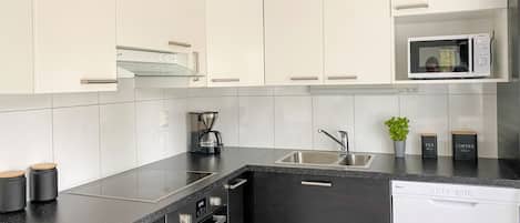 A modern kitchen with white cabinets, a black countertop, a built-in oven, a sink, and a microwave.