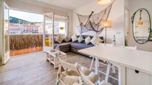 A modern living room with a sofa, dining table, and chairs. There is a large window with a view of buildings and hills. - Beautiful apartment in Calella 5 minutes from the beach. Close to shops and restaurants. Free WIFI. Vivalidays Ilaria. (Calella)