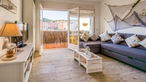 A modern living room with a sofa, a coffee table, a TV, and a balcony with a view of buildings. - Beautiful apartment in Calella 5 minutes from the beach. Close to shops and restaurants. Free WIFI. Vivalidays Ilaria. (Calella)