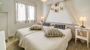 A bedroom with two beds, a bedside table with a lamp, a window with curtains, and wall art. - Beautiful apartment in Calella 5 minutes from the beach. Close to shops and restaurants. Free WIFI. Vivalidays Ilaria. (Calella)