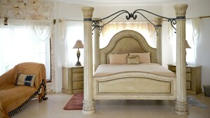 Een hemelbed met een marmeren hoofdeinde, twee nachtkastjes met lampen, een chaise longue en een stenen muur.
