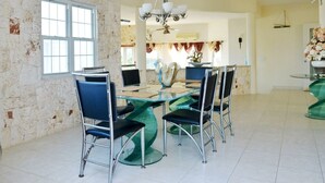 Een eetgedeelte met een glazen tafel en stoelen, een kroonluchter en een stenen muur.