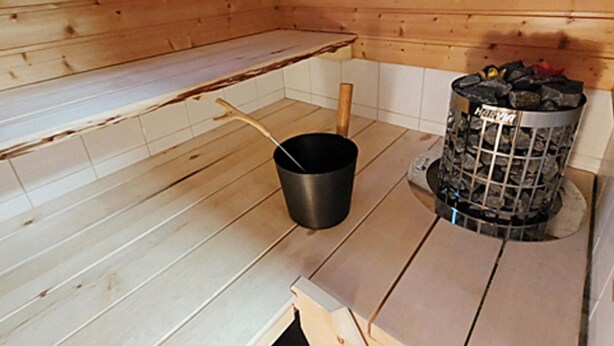 Ein Holzblockhaus-Interieur mit einem Metall-Eimer, einem Holzlöffel und einer Mülltonne mit dem Aufdruck 'Hervia'.