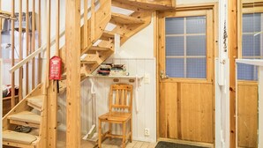 Eine Holztreppe führt zu einem Schlafzimmer auf dem Dachboden, mit einem Fenster, einem Sessel und einem Regal voller Bücher.
