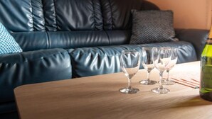 Un sofá de cuero azul oscuro con un cojín, una mesa de madera con tres copas de vino y una botella, y una almohada estampada en el sofá.
