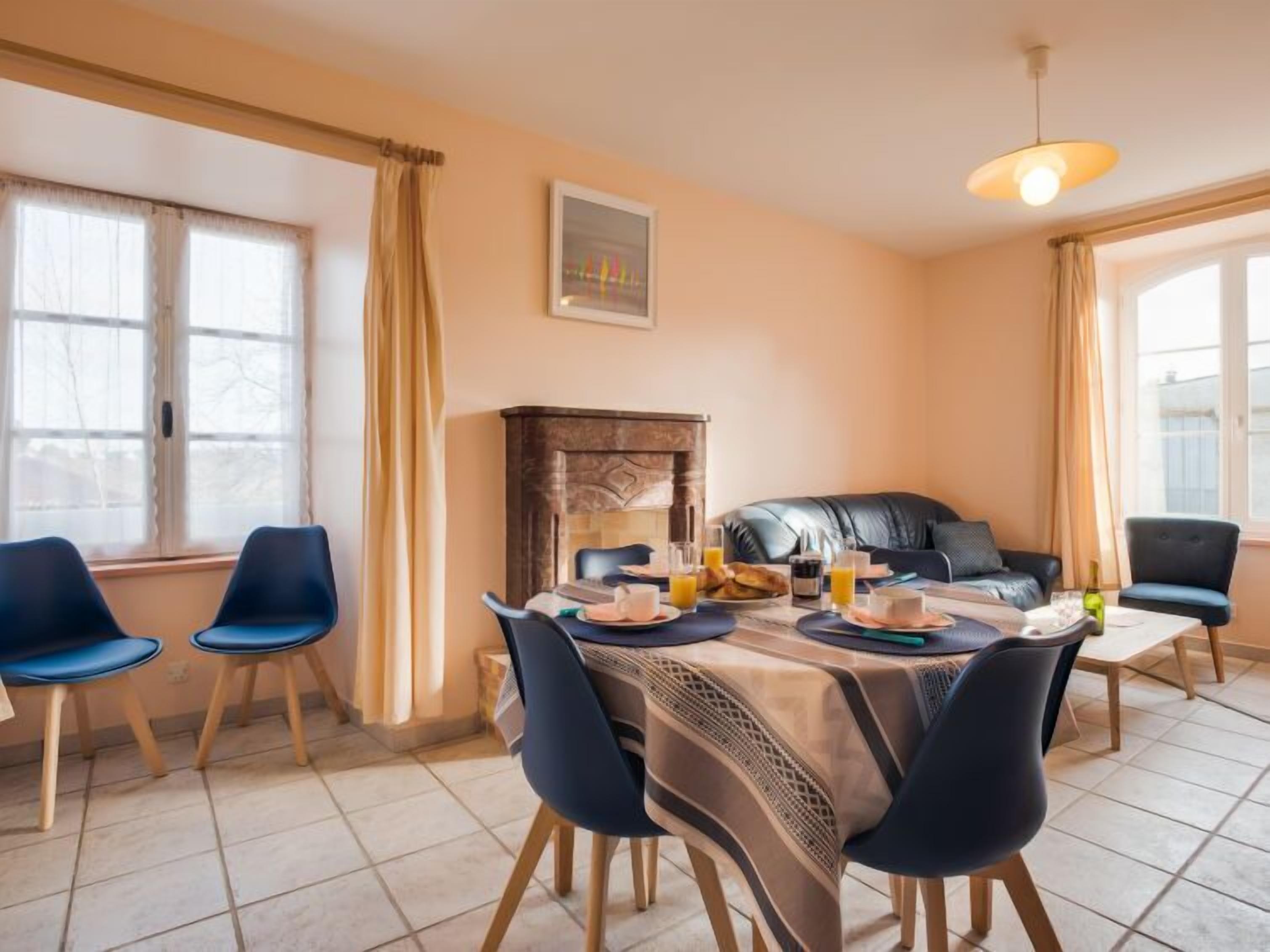 Un comedor con una mesa dispuesta para cuatro, chimenea y vistas al exterior a través de amplios ventanales.