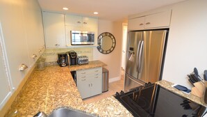 A modern kitchen with granite countertops, stainless steel appliances, a microwave, a clock, and a coffee maker.