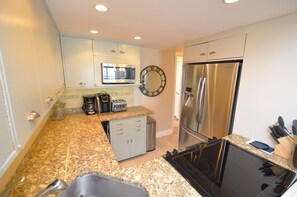 A modern kitchen with granite countertops, stainless steel appliances, a microwave, a clock, and a coffee maker.