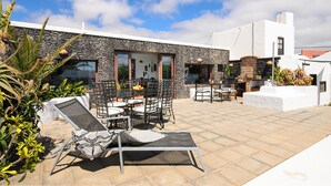 A modern building with a stone facade, outdoor seating area with chairs and tables, and a view of the sky. - Rustic Home Short Drive from Beach with Pool, Terraces & Garden (Güime)