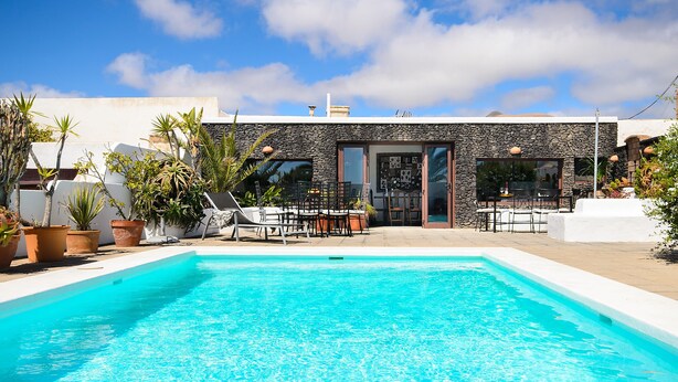 A swimming pool with a stone facade, outdoor seating, and potted plants. - Rustic Home Short Drive from Beach with Pool, Terraces & Garden (Güime)