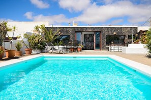 A swimming pool with a stone facade, outdoor seating, and potted plants. - Rustic Home Short Drive from Beach with Pool, Terraces & Garden (Güime)
