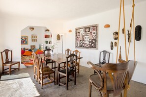 Un coin repas avec une table et des chaises en bois, une balançoire suspendue et un mur orné de divers objets décoratifs.