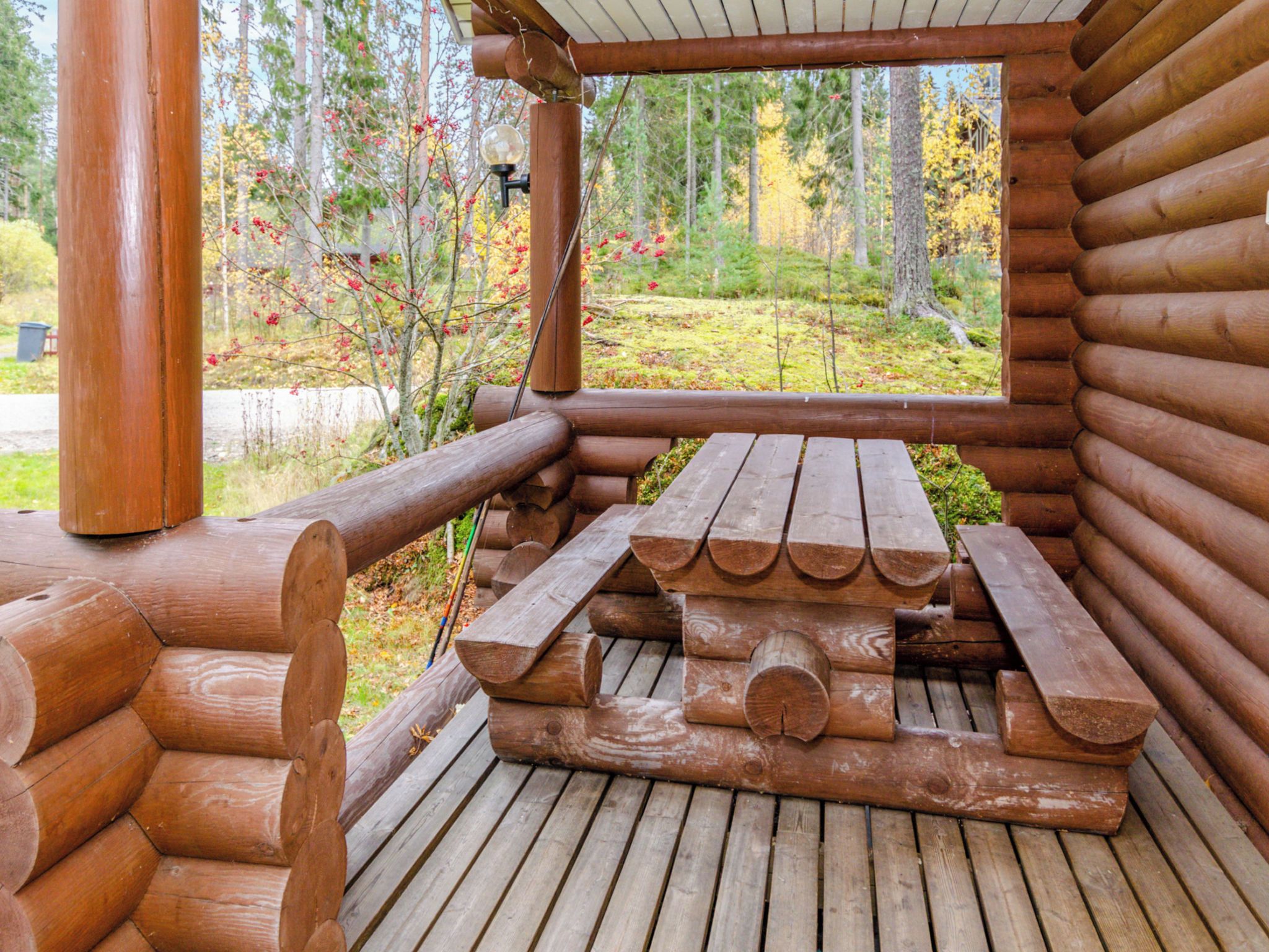 A wooden deck with a picnic table and benches, surrounded by a wooden cabin structure.