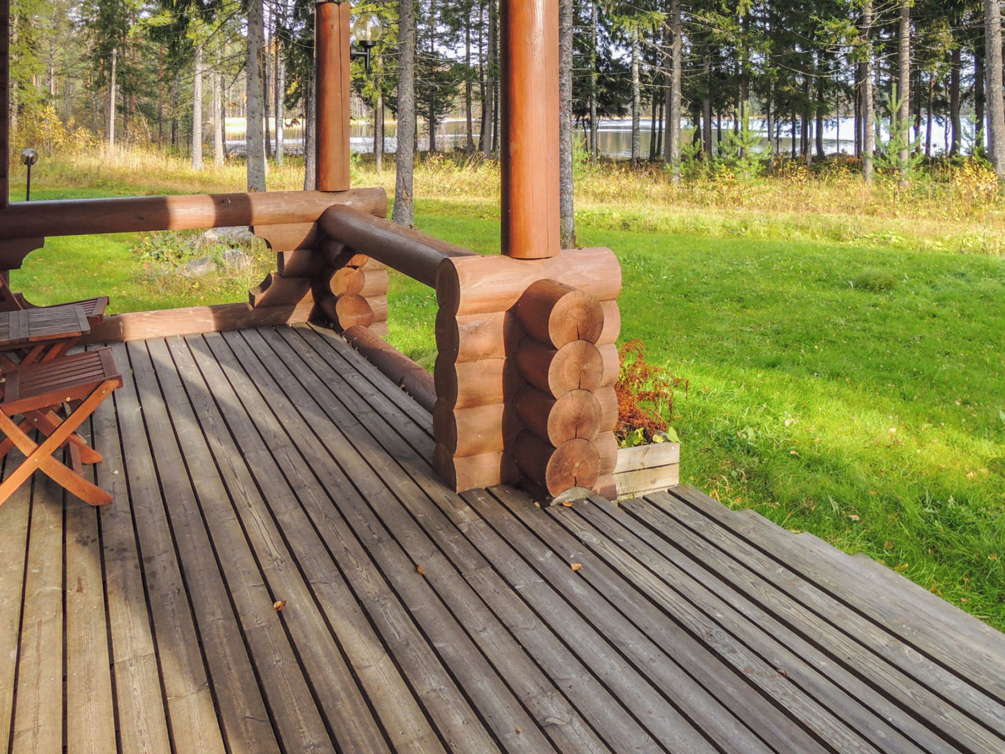 Eine Holzterrasse mit Picknicktisch und Bänken, umgeben von einer Rasenfläche und Bäumen.