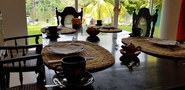 A dining table set with placemats, a teapot, and a cup, with chairs around it.