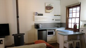 Cocina compacta con estufa, microondas y lavabo. Hay un pequeño comedor con taburetes y un televisor en la esquina.