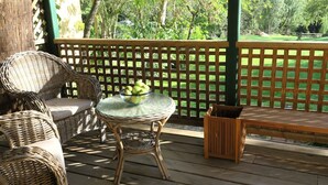 Un espacio de estar al aire libre cubierto con mobiliario de mimbre, una mesa de vidrio con un frutero y vistas a un paisaje verde.