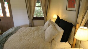 Una cama bien hecha con ropa de cama blanca, un almohadón negro y una lámpara dorada sobre una mesita de noche.