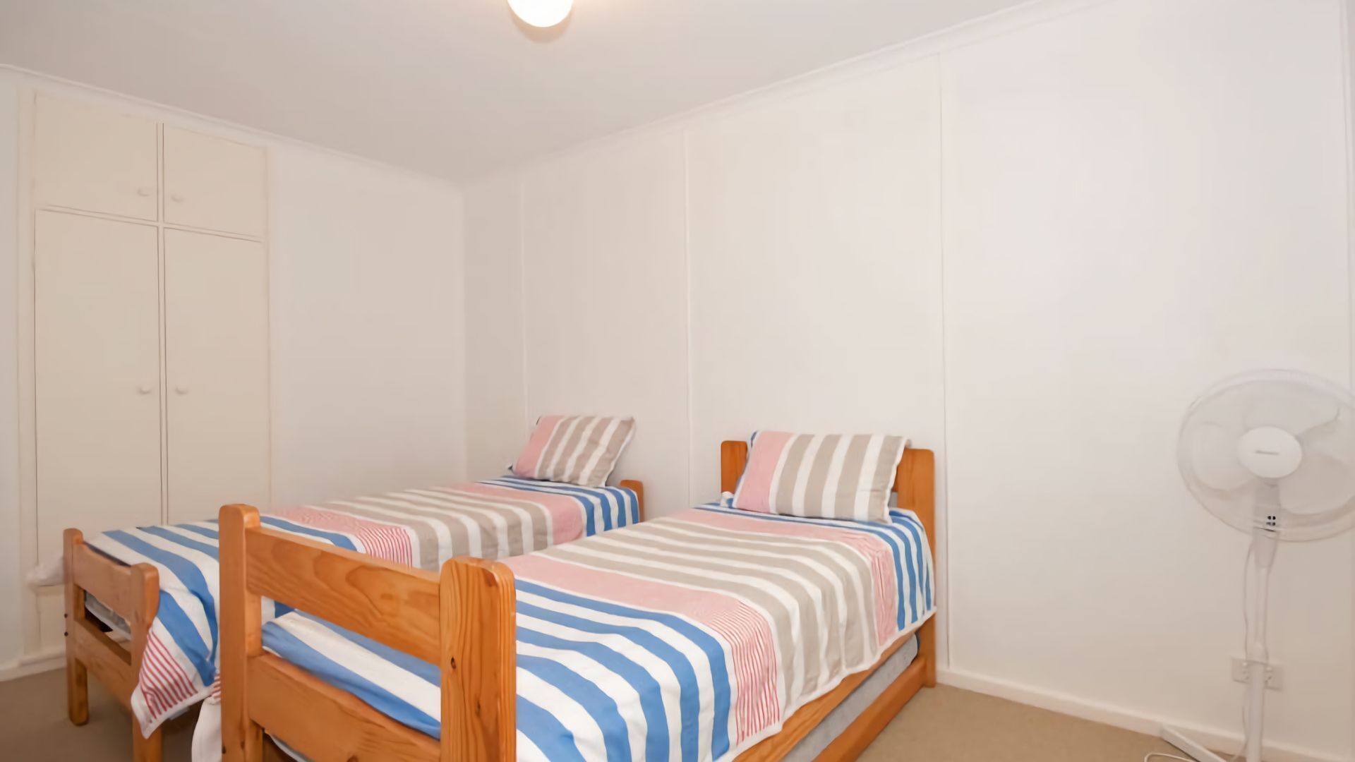 Un dormitorio con dos camas individuales, cabeceros de madera y un ventilador blanco.