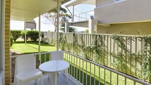 A balcony with a white table and chairs, a view of a well-maintained lawn, and a wooden fence. - Beachside Shoal Bay Unit 4 (Shoal Bay)