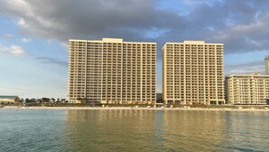 Un hotel moderno de gran altura con varios pisos y balcones, situado cerca de una playa con aguas tranquilas que reflejan los edificios.